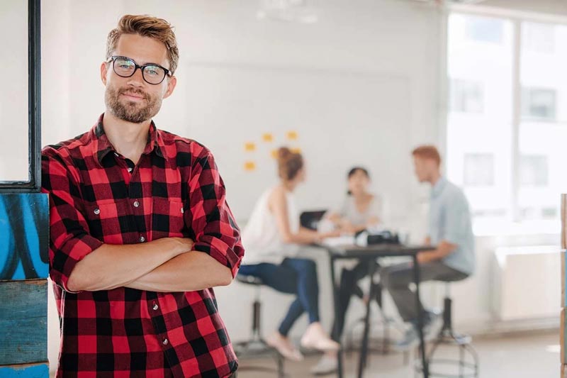 Man standing in office with colleagues in background discussing how to create highly engaging content
