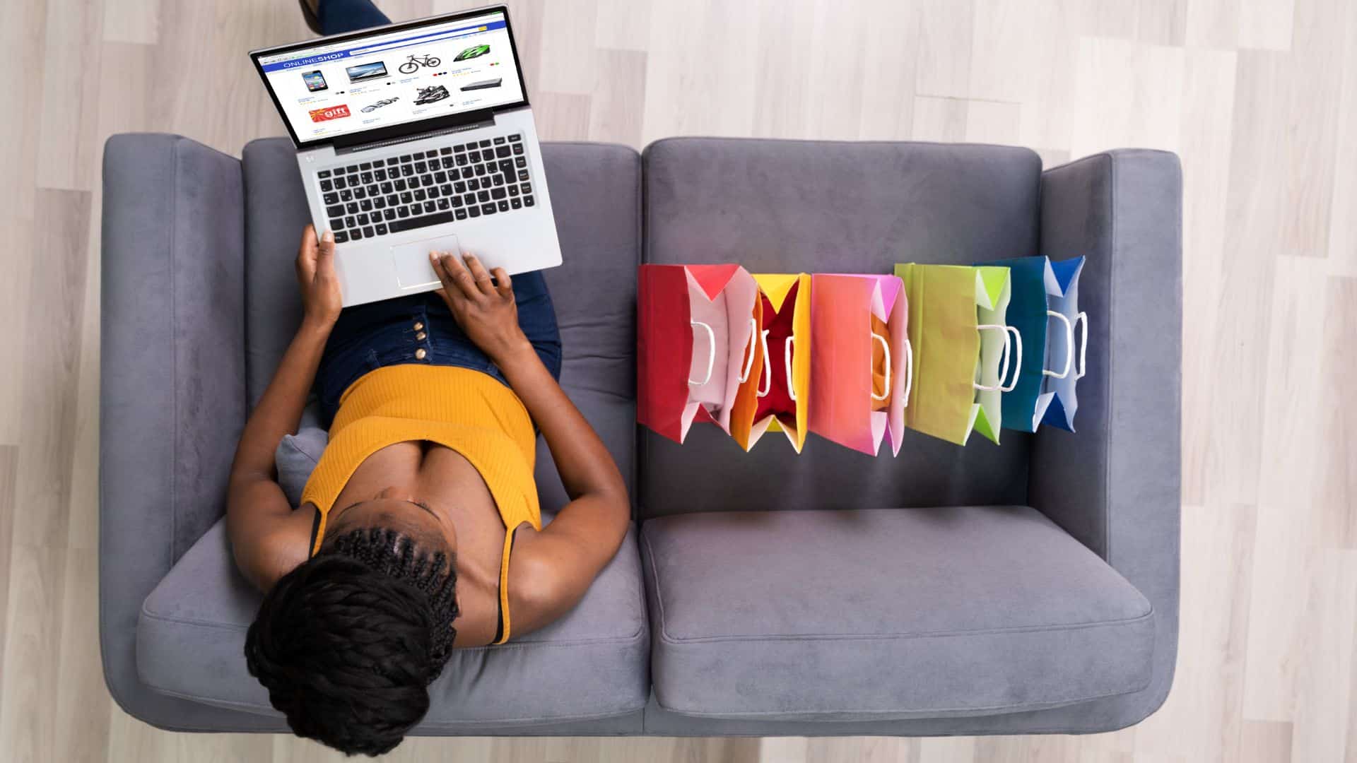 Woman sitting on couch purchasing products from her laptop with multiple bags next to her