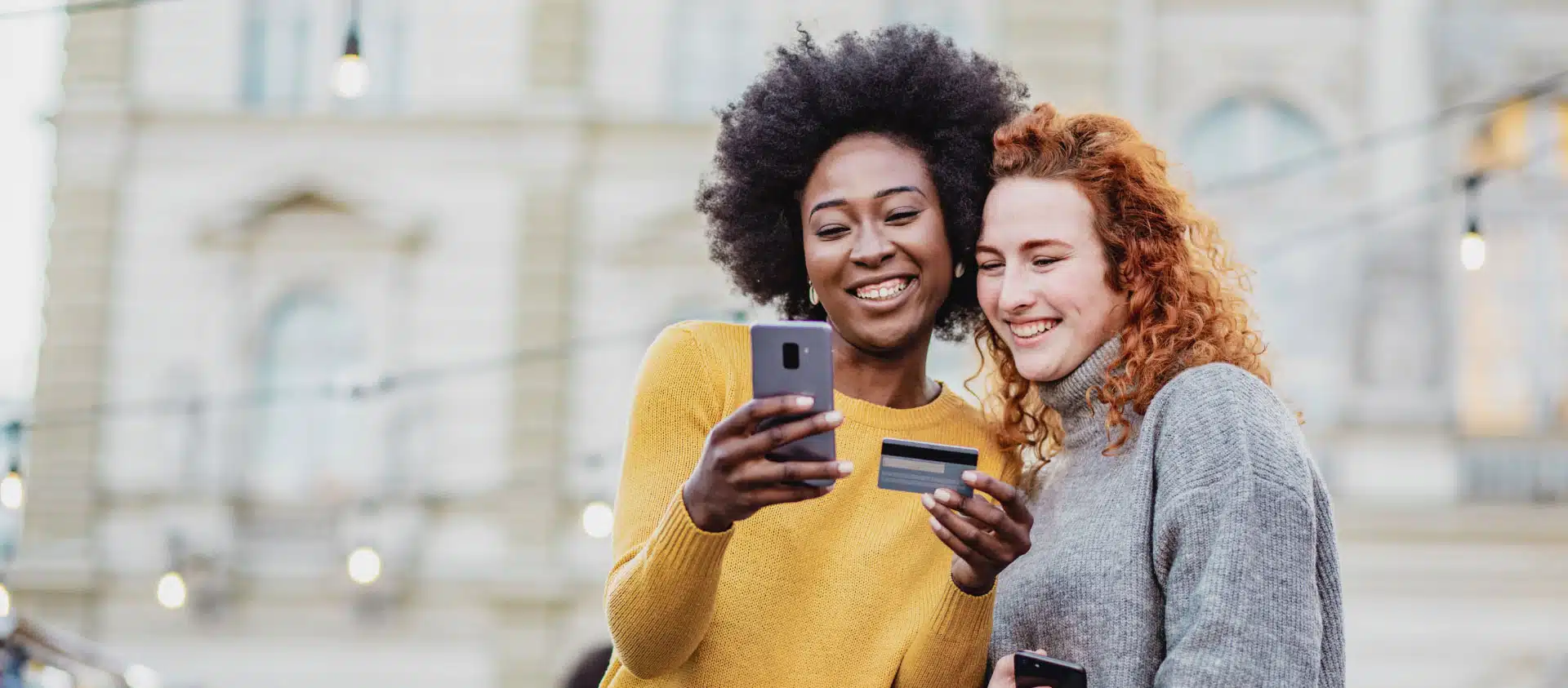 Two people laughing looking at their phone’s with a credit card in hand